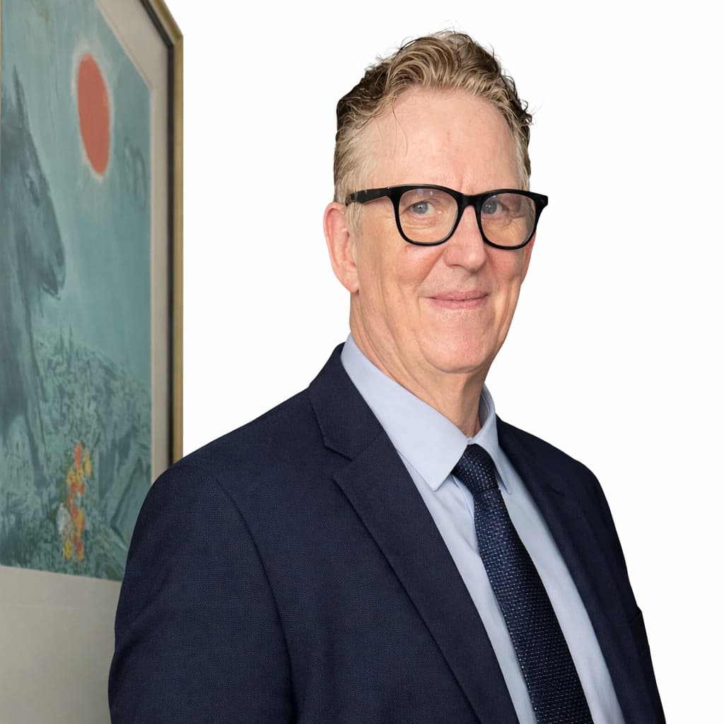 Man in glasses and a blue suit smiling, posing next to a framed artwork.